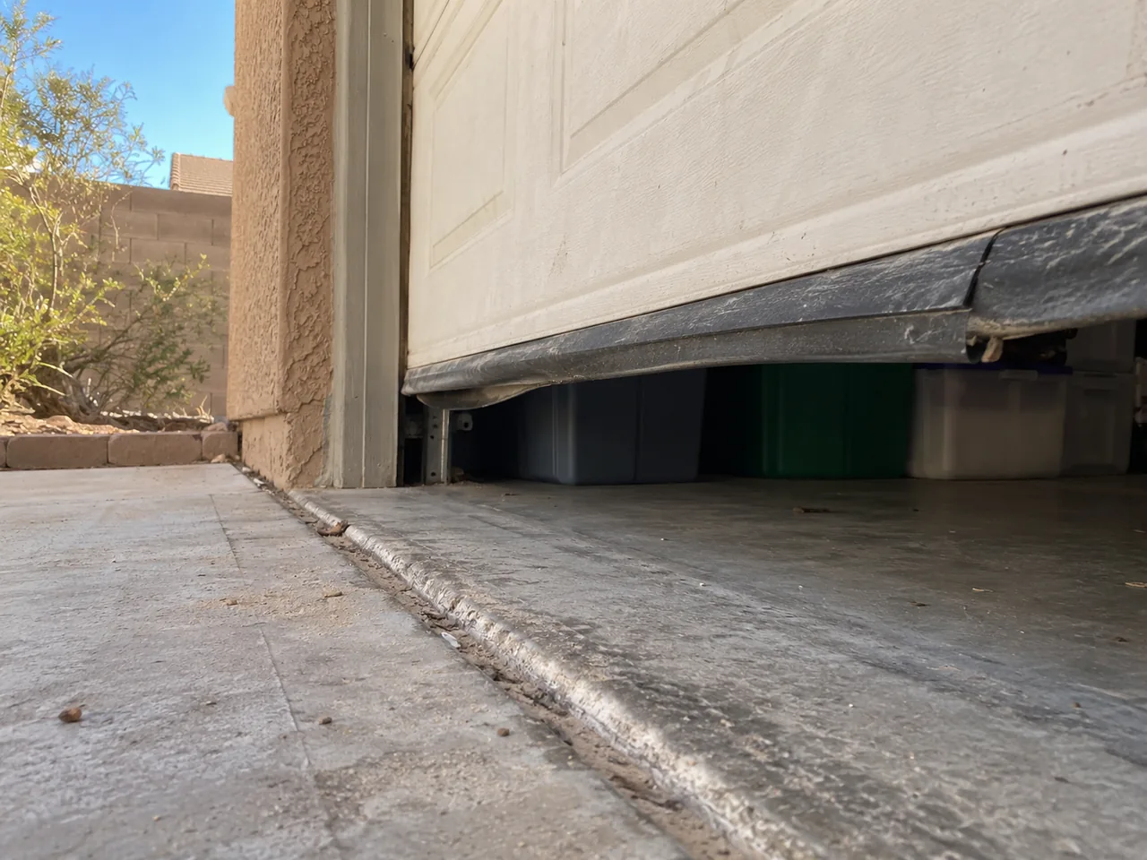 Worn garage-door bottom seal and concrete threshold at a stucco house